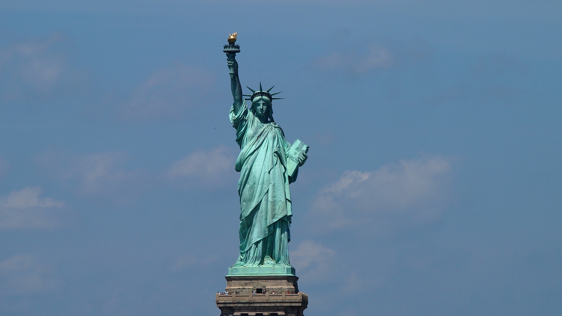 a tall clock tower sitting under a cloudy blue sky with Statue of Liberty in the background