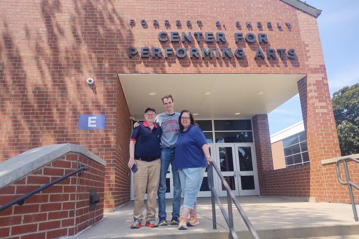 Three people standing in front of a performing arts center entrance.