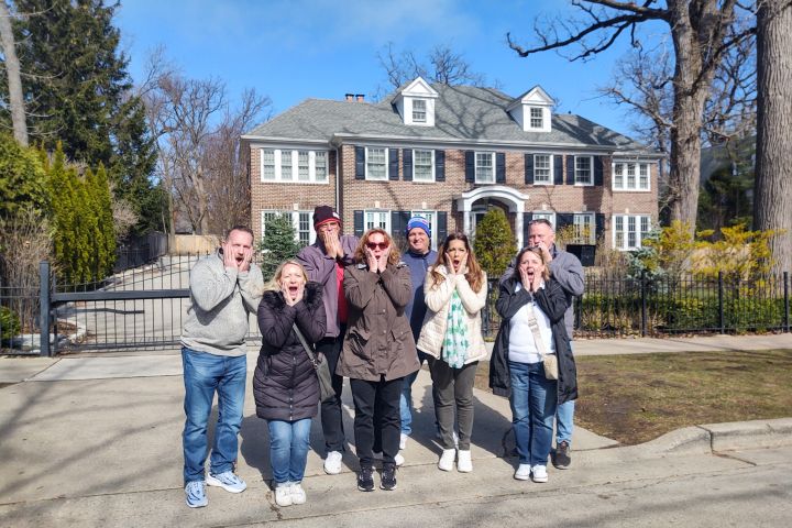 Group posing with shocked expressions in front of a large brick house.