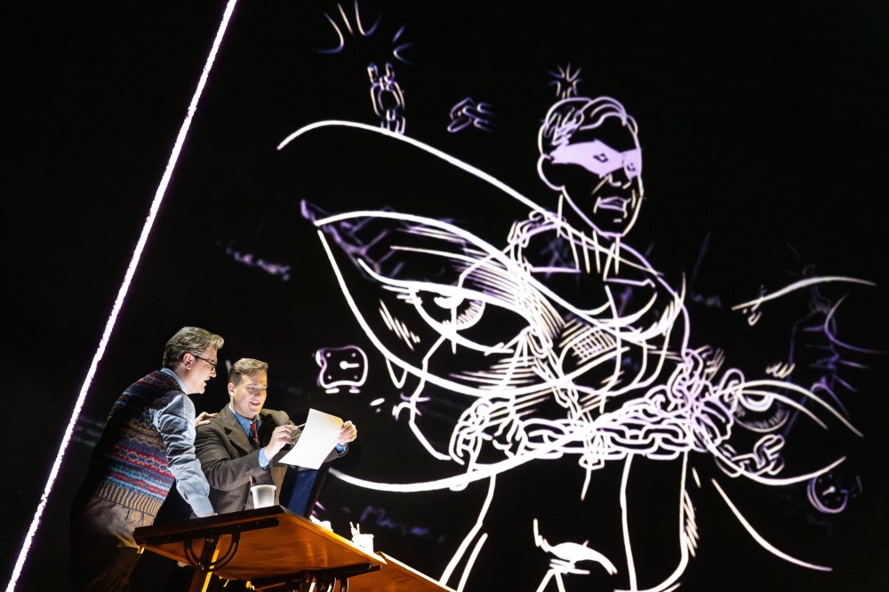 Two people at a desk with a large abstract illustration projected behind them.