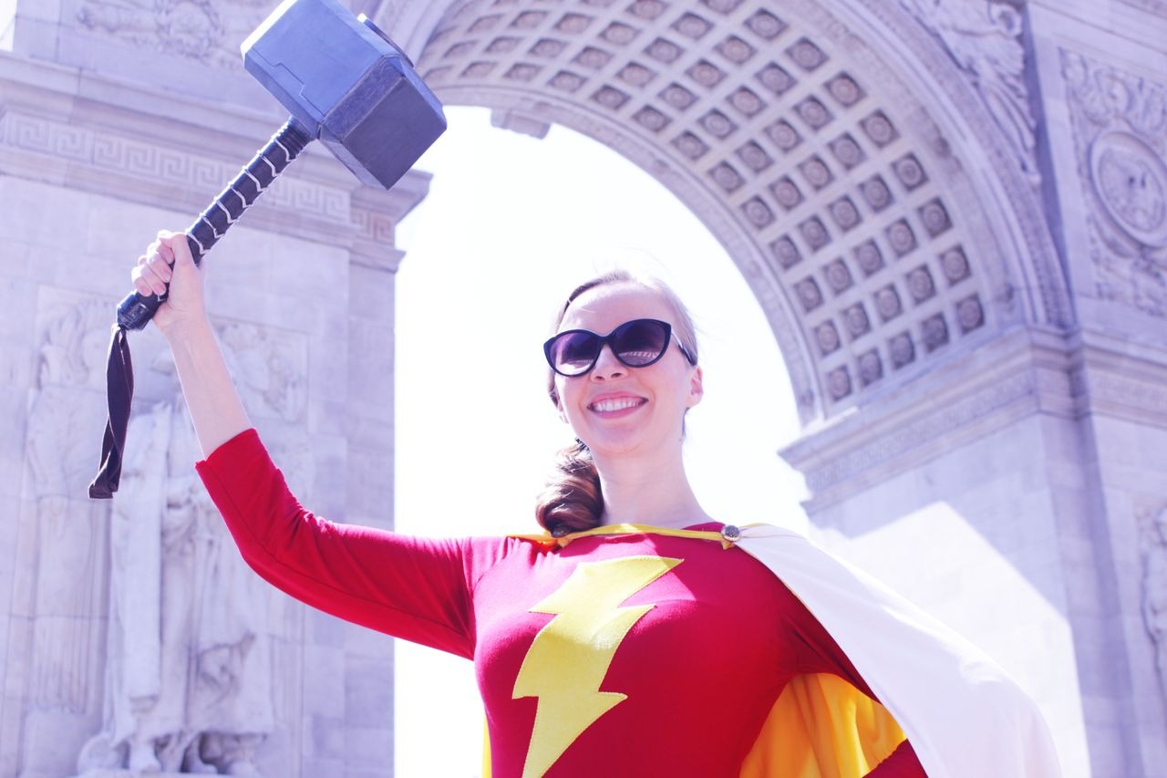 Person in superhero costume holding a hammer with archway background.